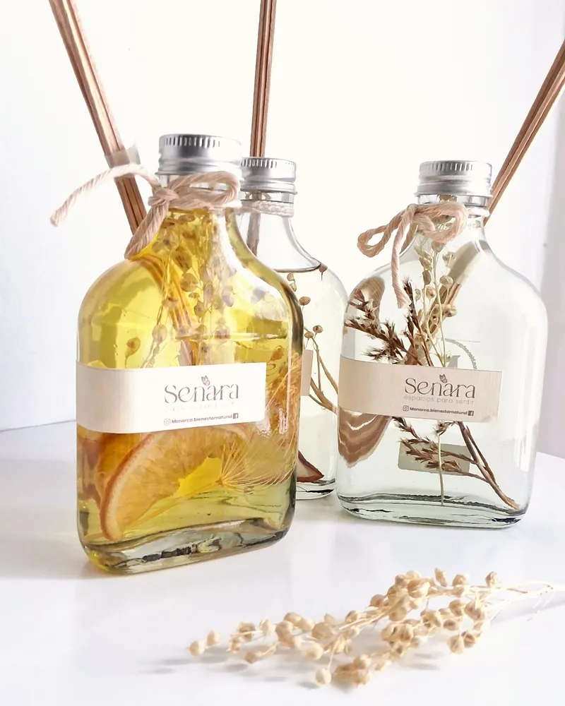 Tres difusores de varillas Senara, uno con aceite amarillo y rodajas de naranja, con flores secas, junto a un ramito seco